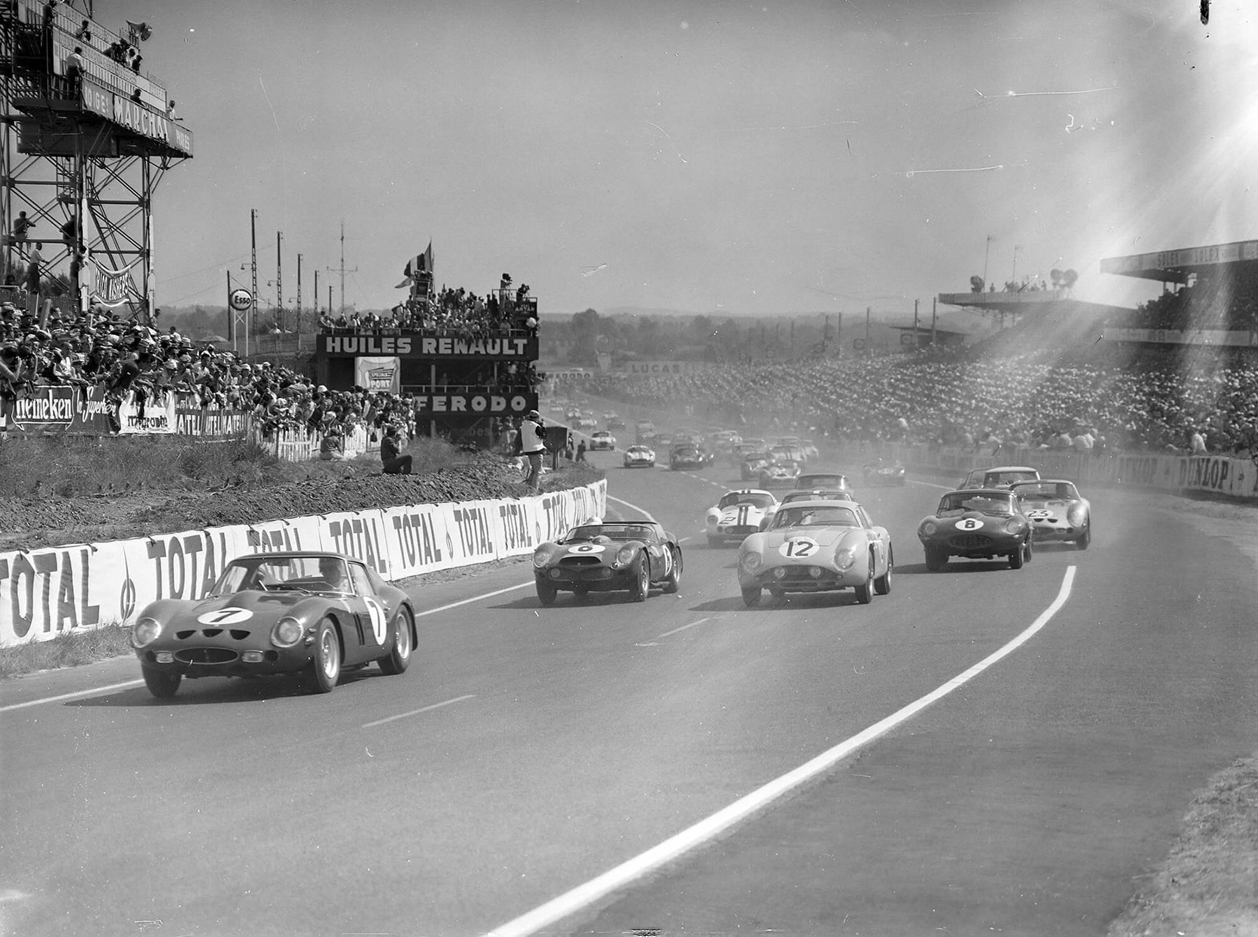 Mike Parkes and Lorenzo Bandini’s Ferrari, chassis no. 3765 (#7), leads Jean Kerguen and Jacques Dewes’ Aston Martin (#12), Olivier Gendebien and Phil Hill’s Ferrari (#6), and Maurice Charles and John Coundley’s Jaguar (#8) at the start of the 24 Hours of Le Mans at Circuit de la Sarthe on 24 June 1962.