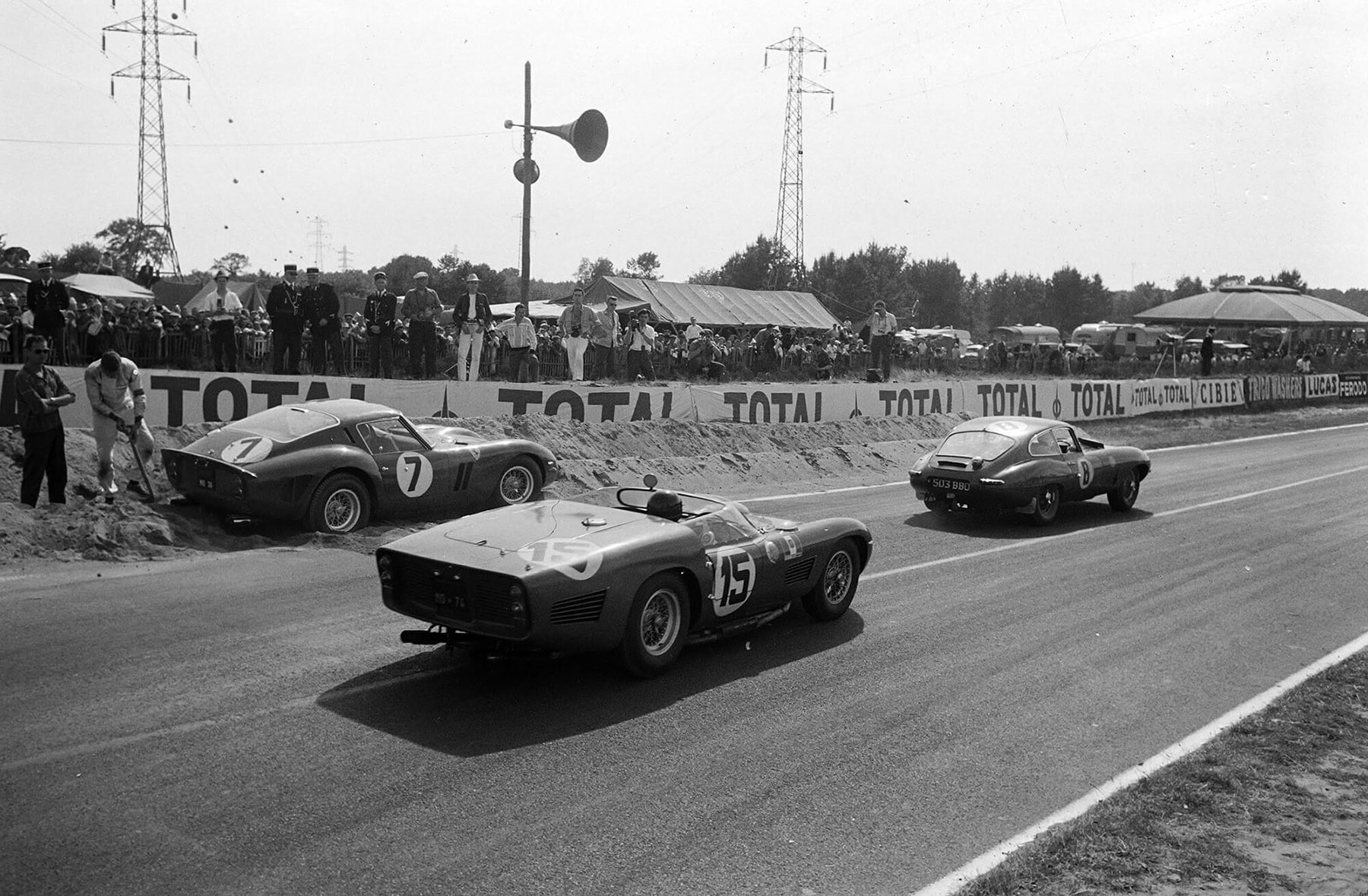 Maurice Charles and John Coundley’s Jaguar E-type (#8), leads Joakim Bonnier and Dan Gurney’s Ferrari 250 TRI/61 (#15) past Mike Parkes and Lorenzo Bandini’s Ferrari (#7) beached by the side of the track during the 24 Hours of Le Mans at Circuit de la Sarthe on 24 June 1962.